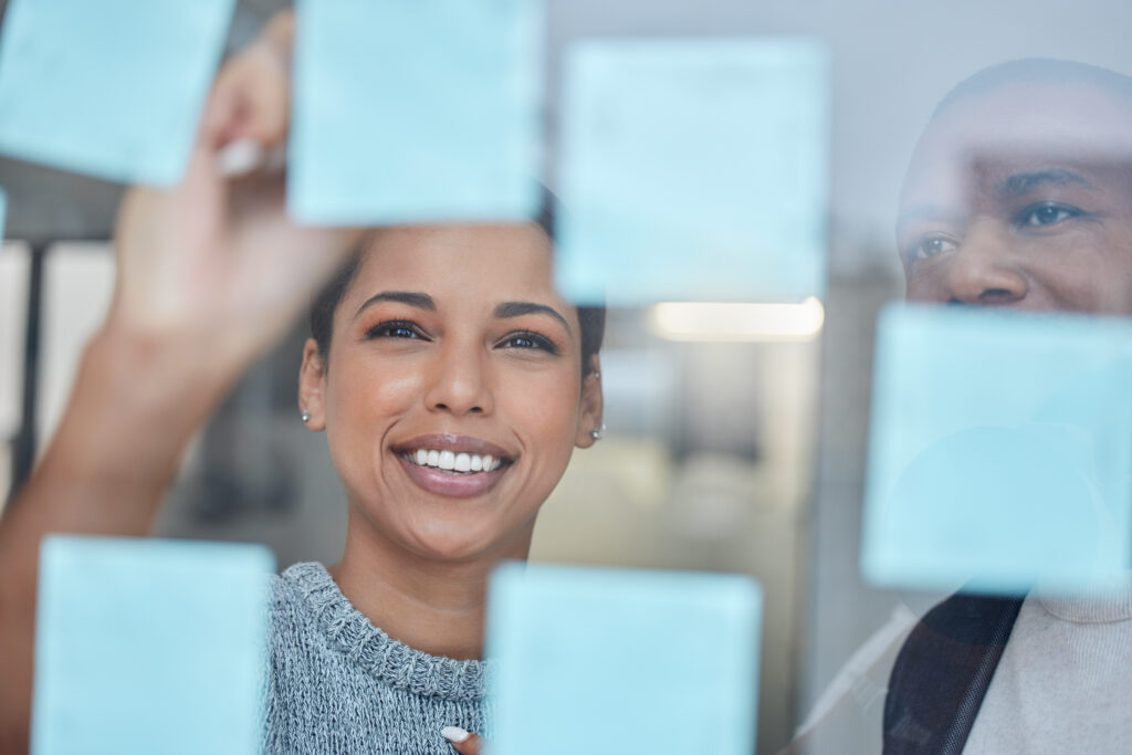 Shot of two businesspeople brainstorming with notes on a glass wall in an office.
