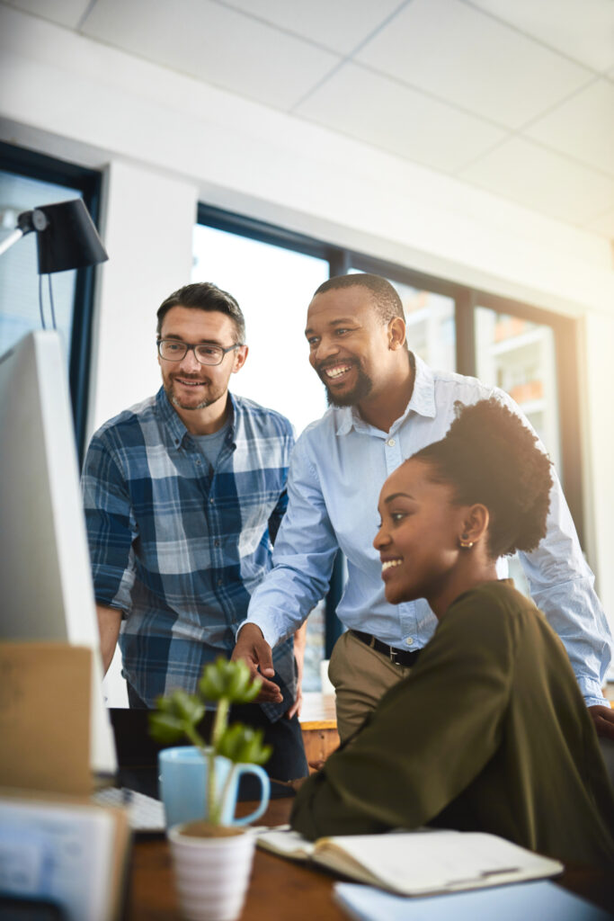 People, computer and happy in office for advice, company review and feedback at creative agency. Journalist team, diversity and technology at table for reading, brainstorming and good news in city.